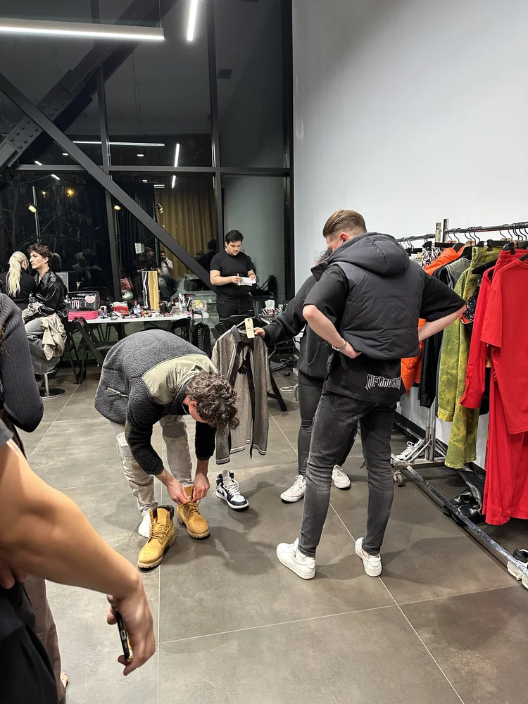 Backstage fitting moment with stylists and models preparing looks before a runway show.