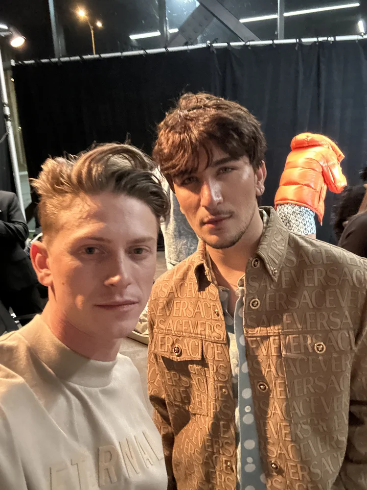 Benjamin Wills backstage during fashion week with a model in a Versace look.